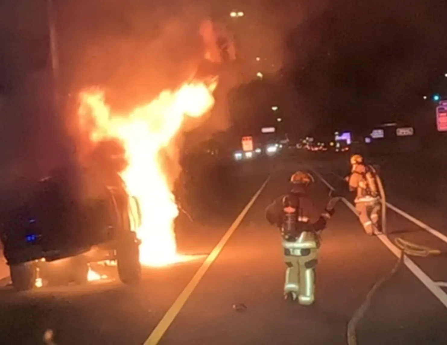 Two firefighters fighting a car fire at night