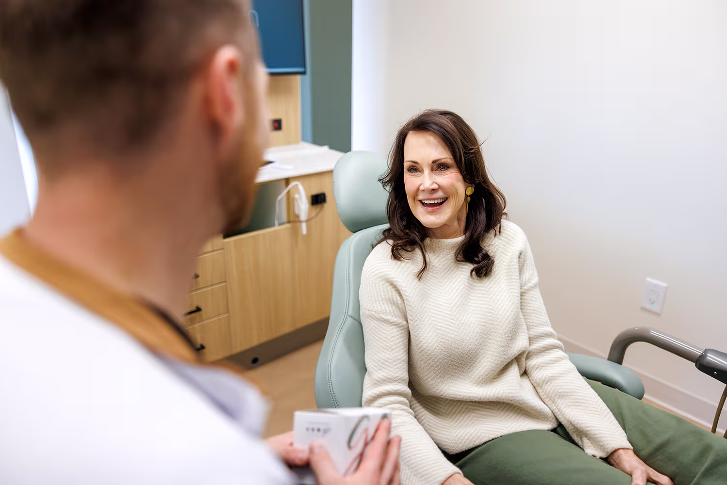 Smiling dentist looks at a male patient holding a hand mirror to check his teeth in a dental office.