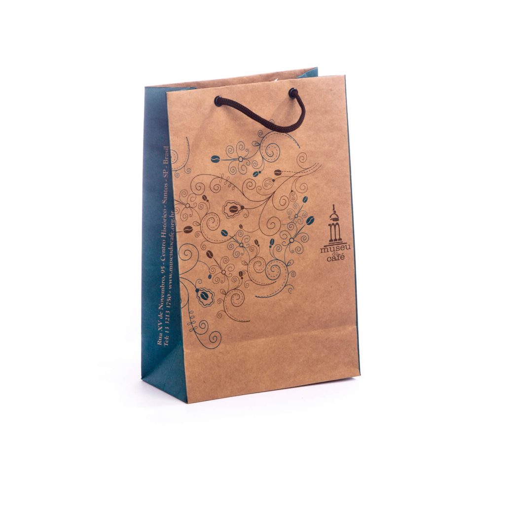 Brown paper shopping bag with decorative swirly coffee bean patterns and Museu do Café logo, navy blue sides, and brown rope handles.