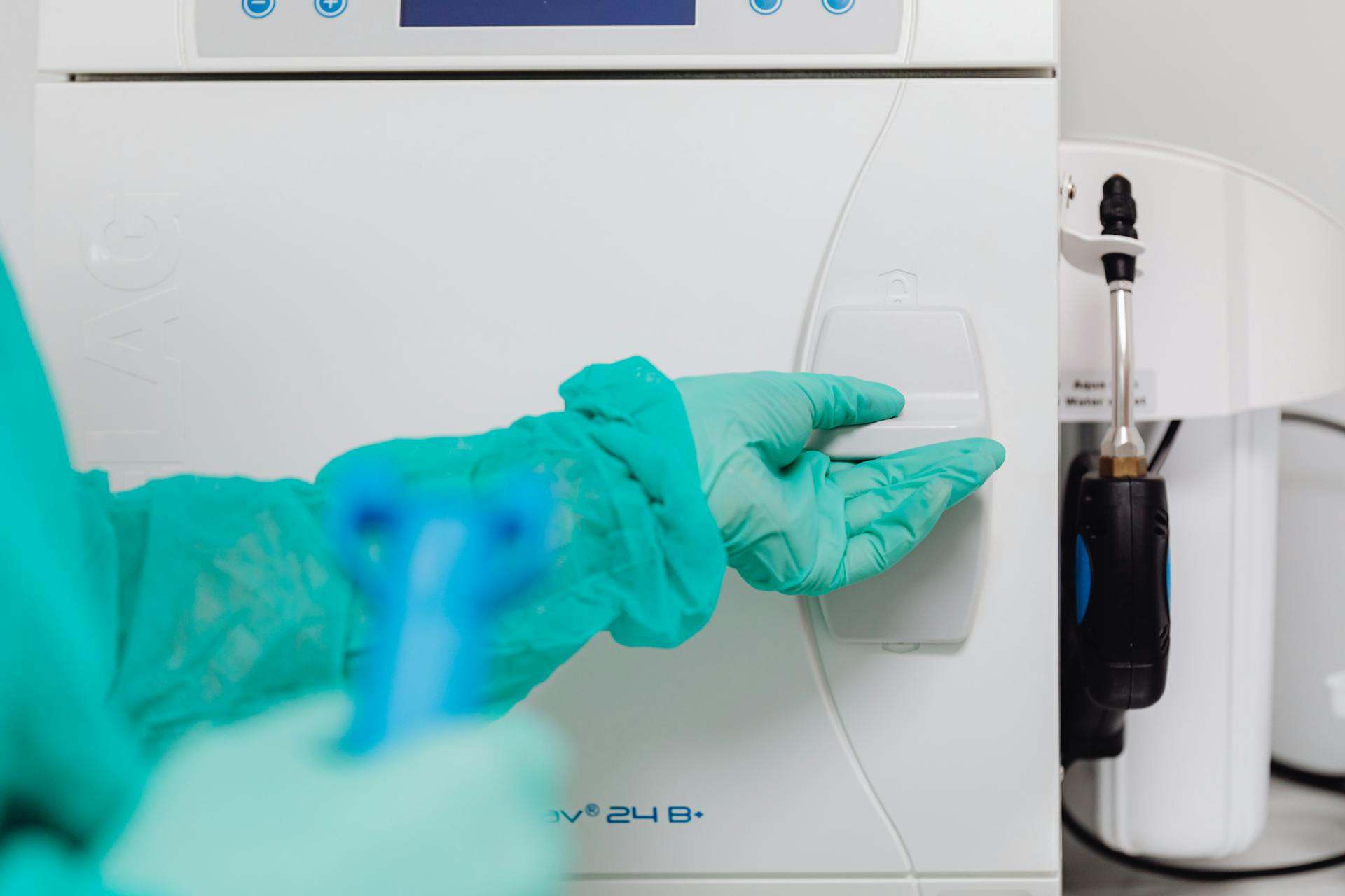 Person wearing teal protective gloves operating a white medical or laboratory device.