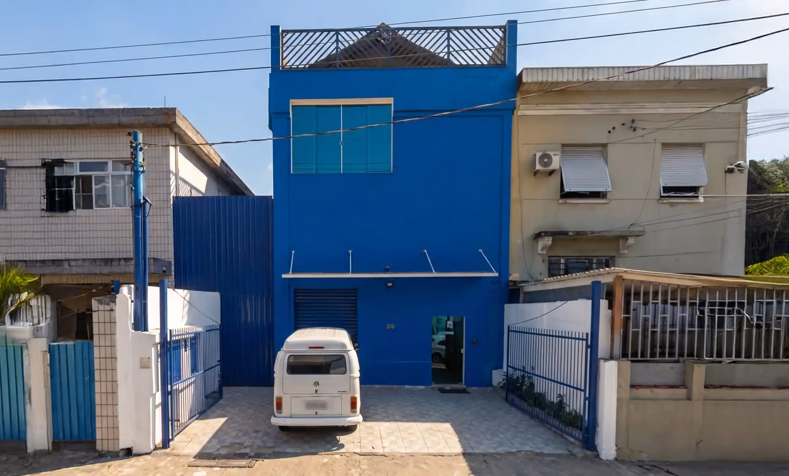 White van parked in front of a two-story blue building with a gated driveway on a sunny day.