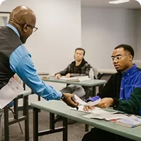 Instructor distributing documents to students in a classroom during CDL training.