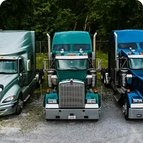 Three semi-trucks parked side by side at a trucking facility.