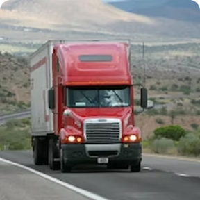 Red semi-truck driving on a highway through a rural landscape.