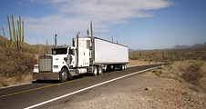 White semi-truck with a box trailer driving on a highway through a dry landscape, representing truck rollover prevention training.