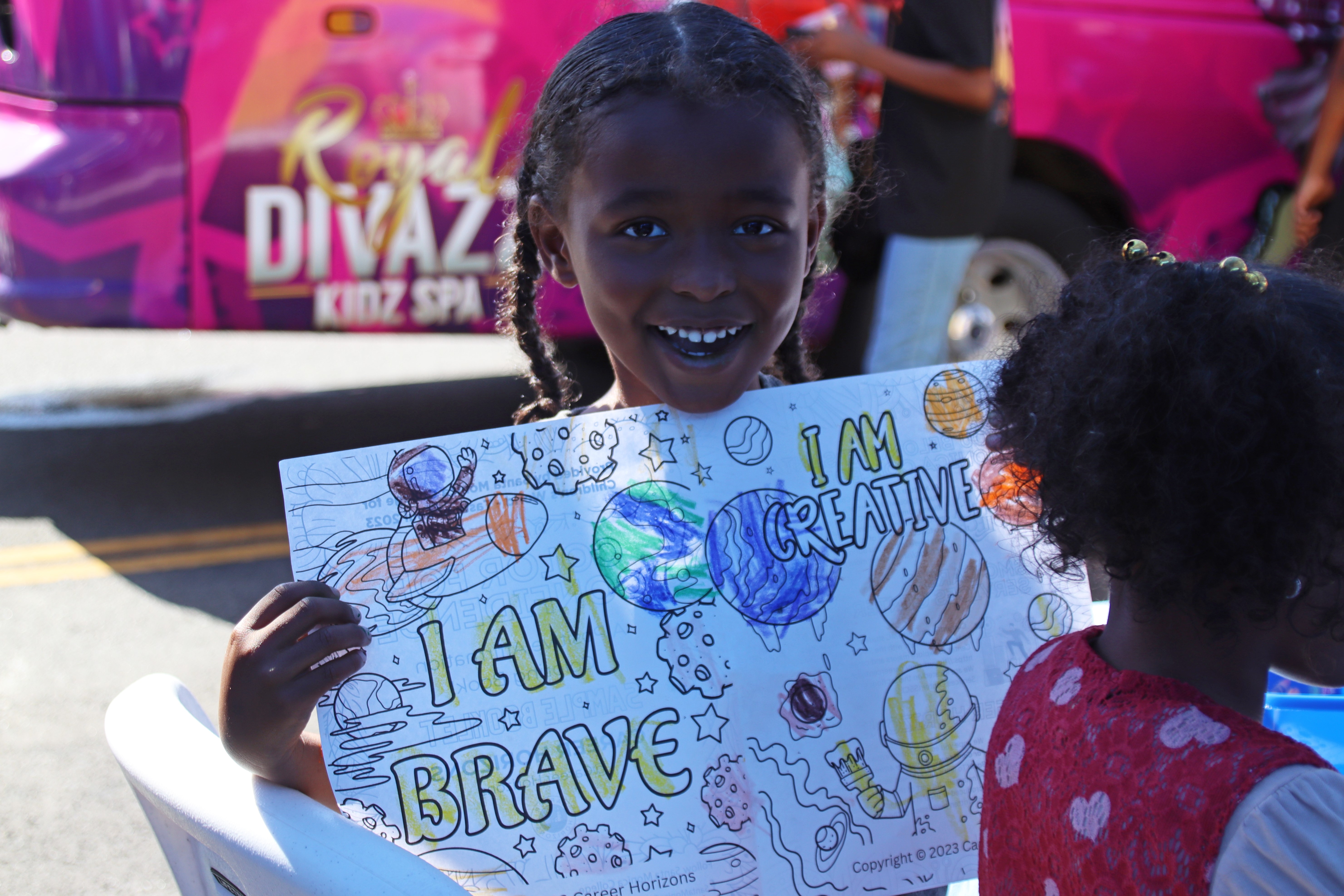 Smiling student holding a colorful “I Am Brave, I Am Creative” coloring page.