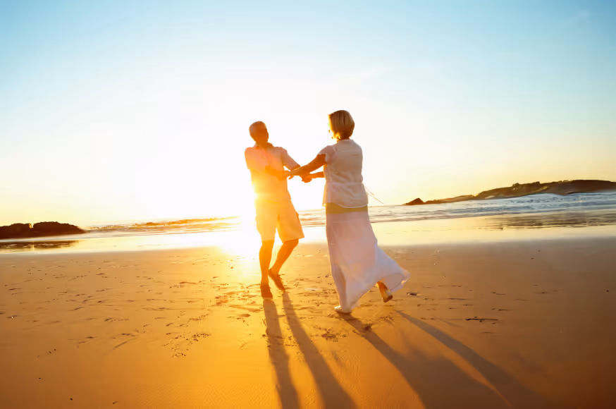 Happy couple holding hands and spinning on a sunlit beach at sunset.