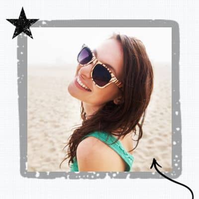 girl in glasses at the beach smiling over her shoulder, representing Invisalign This Summer