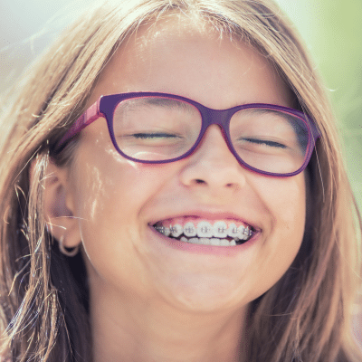 Little girl wearing glasses and smiling with braces, representing crossbites and open bites