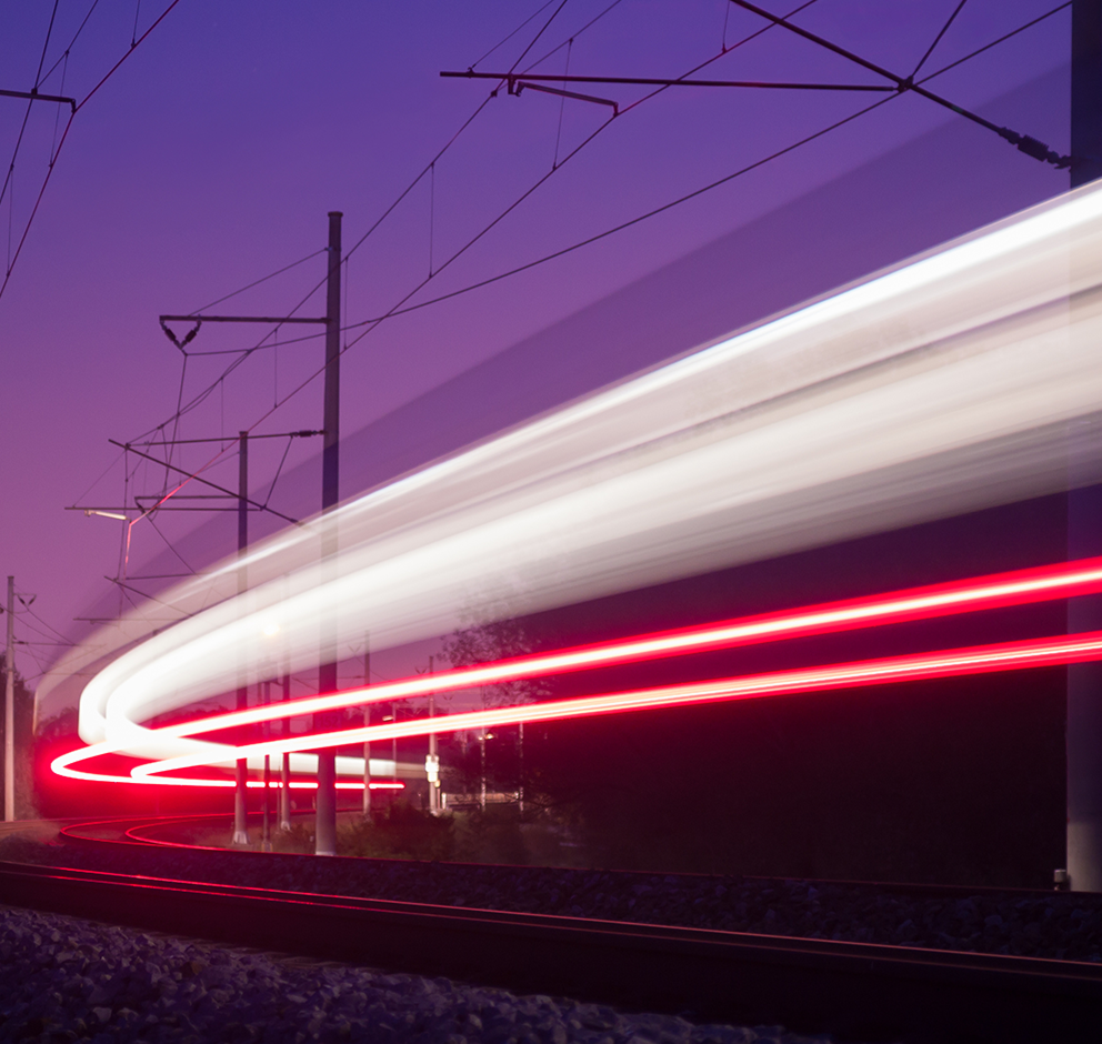 Train lights blur in motion along curved tracks under a twilight sky.