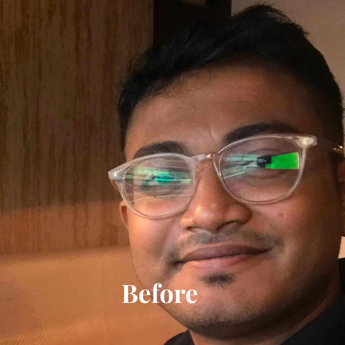 Close-up of a man wearing clear glasses smiling slightly with a wooden background.