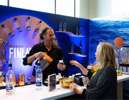 A mixologist serves a sample cocktail to an attendee at a Finlandia Vodka activation booth featuring a blue ocean-themed backdrop