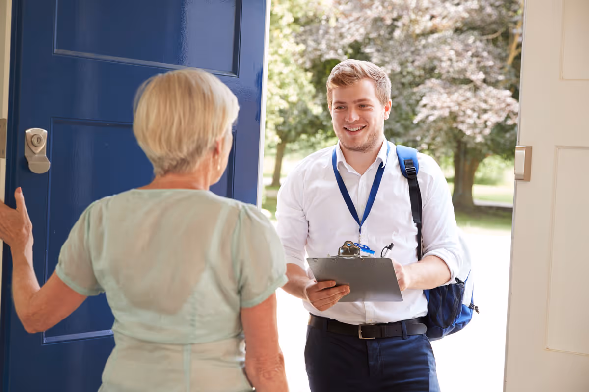 In-person sales associate at a woman’s door, smiling with a clipboard.