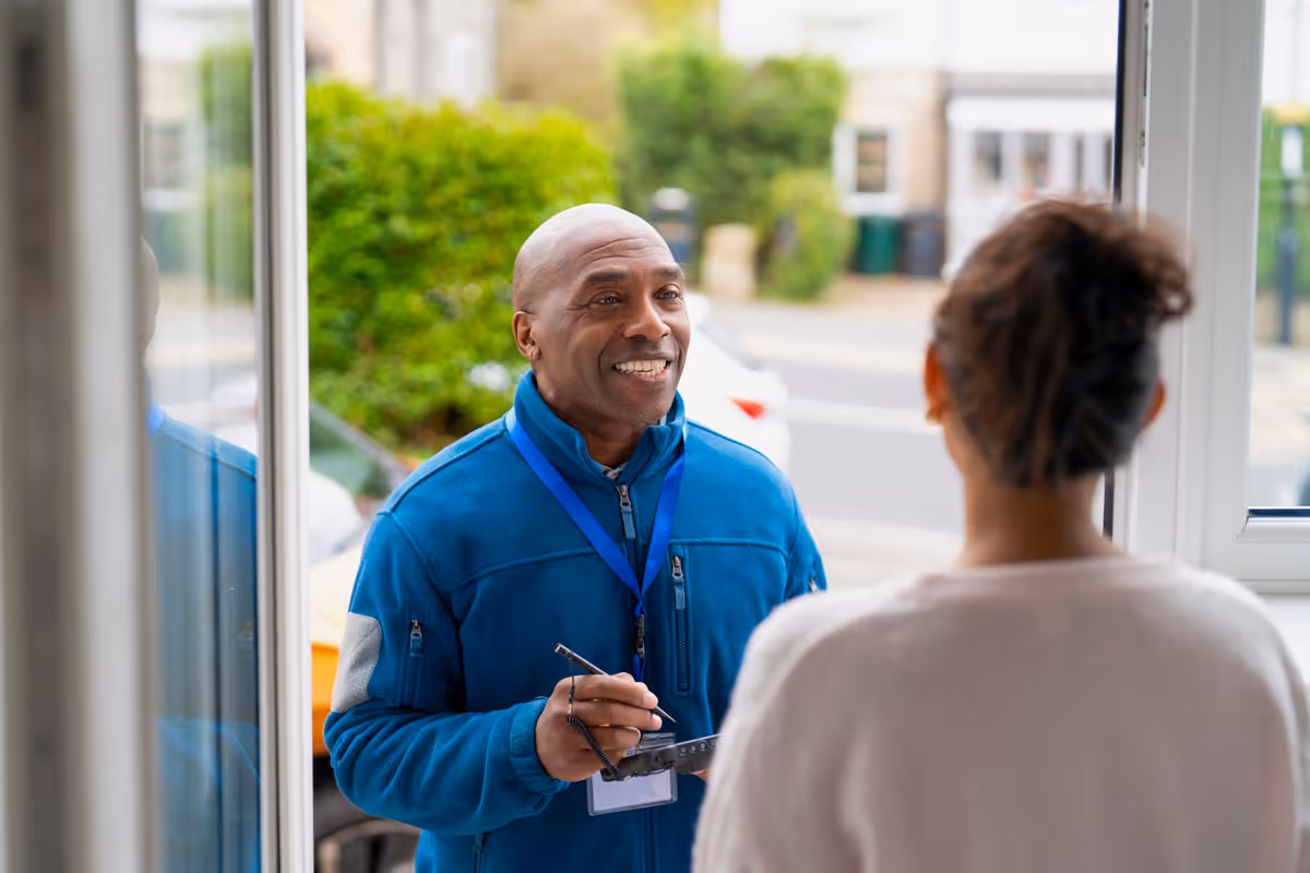 Field sales representative in a blue jacket smiling at a woman at her door, symbolizing what Cydcor does.