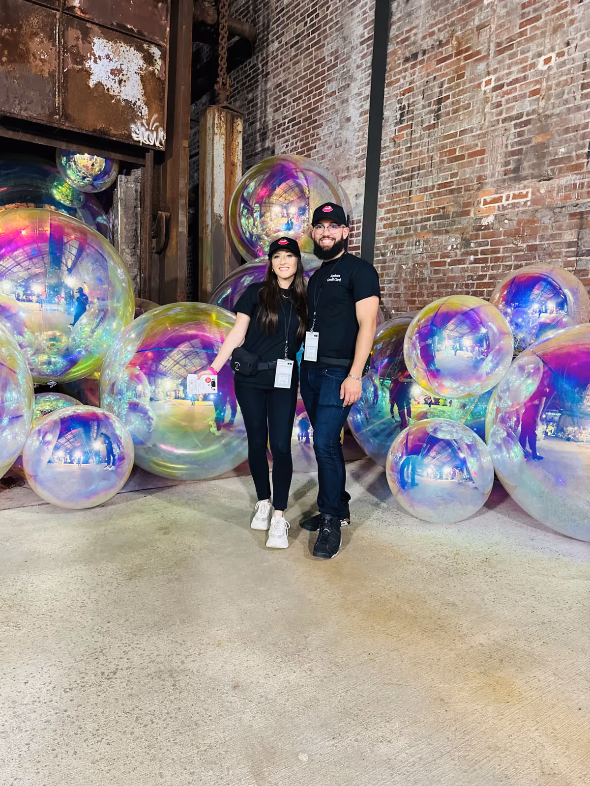 Two smiling event services brand ambassadors standing in front of an abstract decoration piece for an experiential sales event.