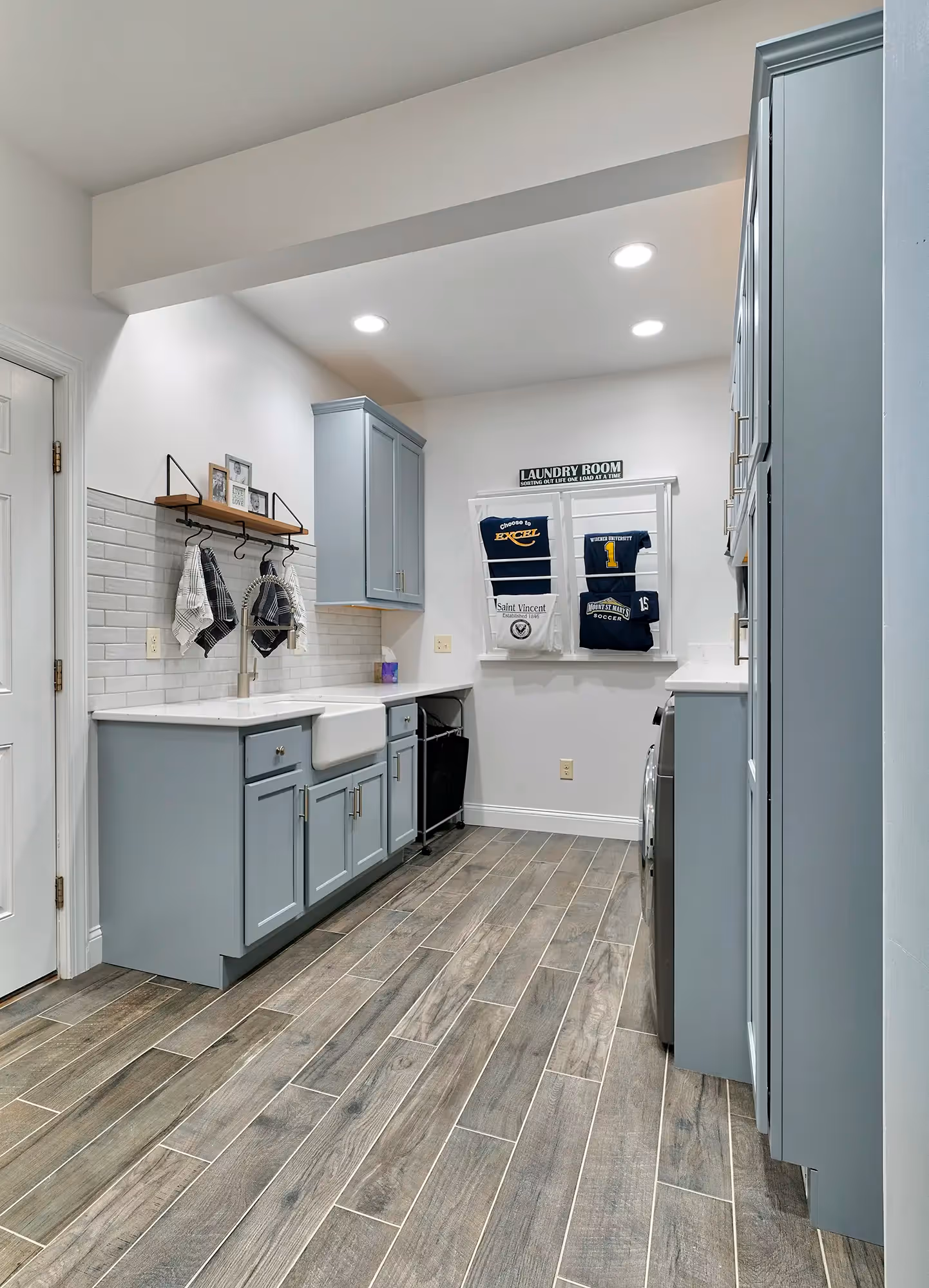 Modern laundry room in Mechanicsburg, PA with blue cabinets, farmhouse sink, and decorative wall hangings.