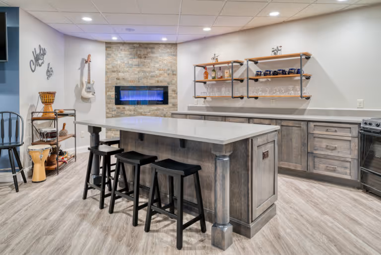 Modern basement kitchen in Mechanicsburg, PA featuring a sleek bar area with gray cabinetry, stainless steel appliances, and a stone accent wall.