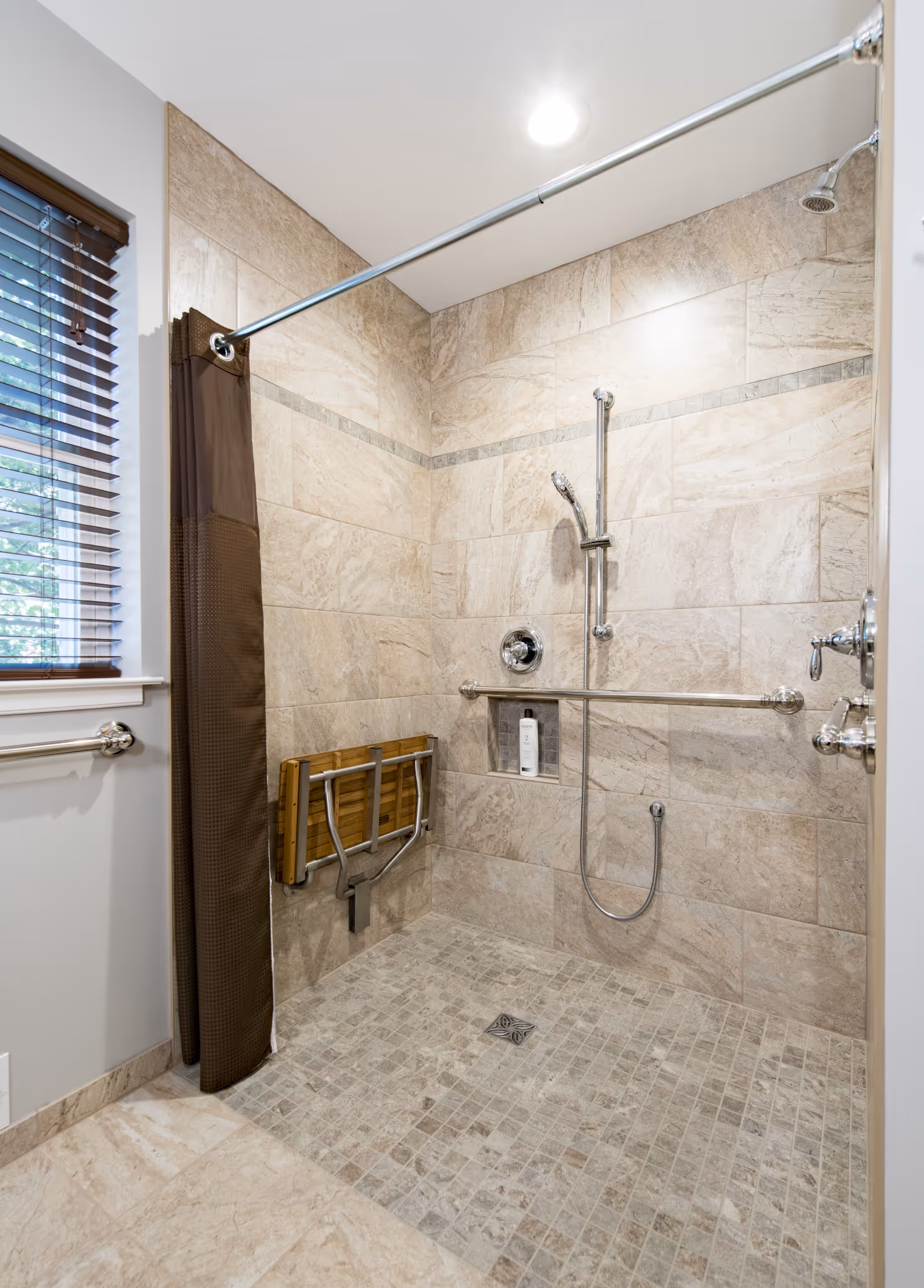 Accessible modern bathroom with beige tile, grab bars, and a folding bench in New Cumberland, PA