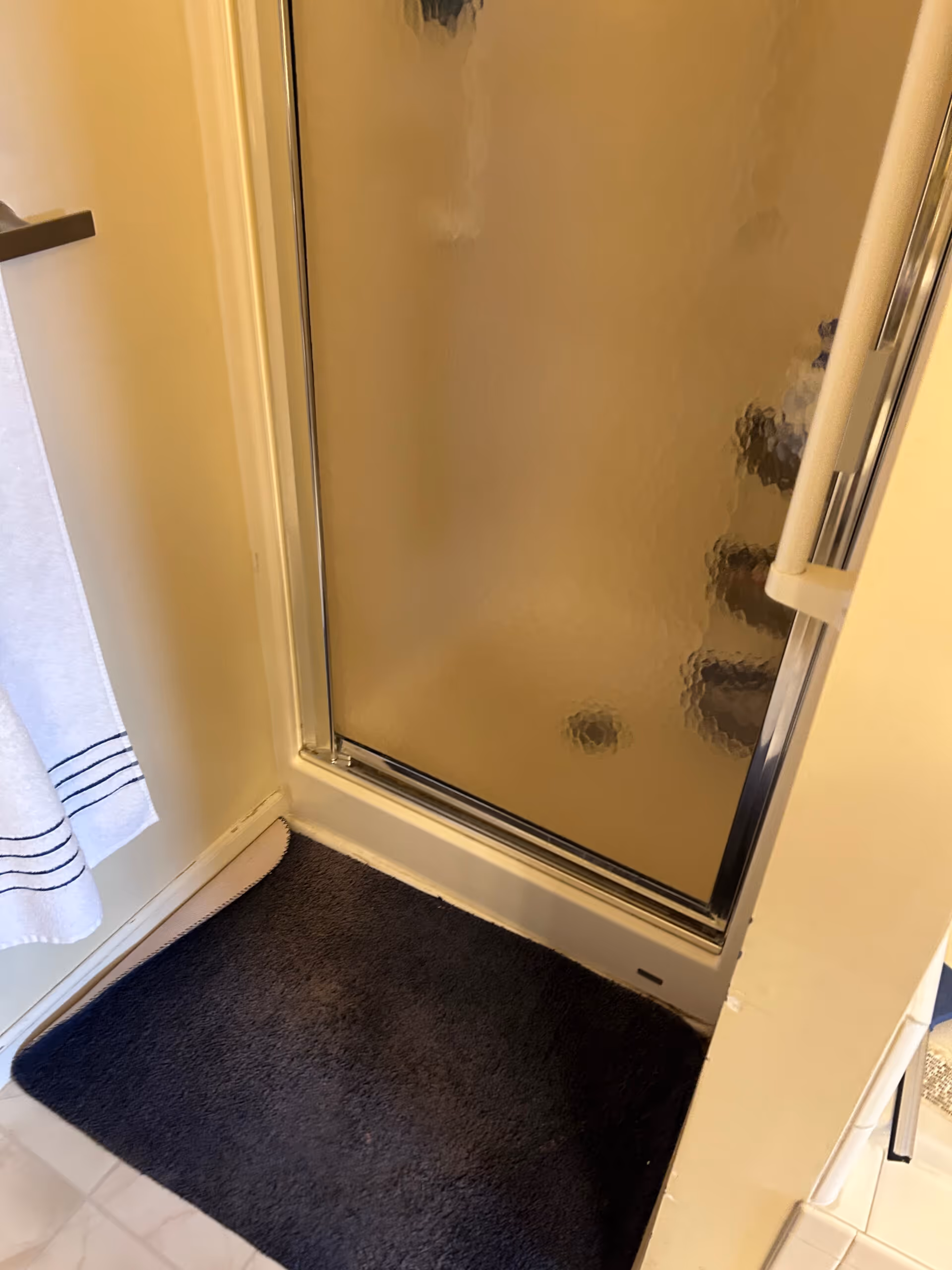 Primary bathroom shower area featuring a glass door and dark bath mat in a remodel project located in harrisburg, pa.