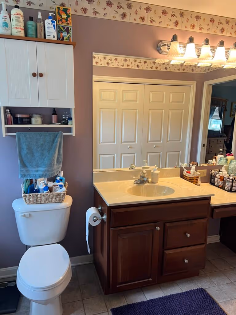 Cozy traditional bathroom in Etters, PA featuring a wooden vanity, floral wallpaper, and a well-organized shelf.