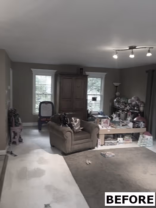 A cluttered living room in New Cumberland, PA featuring a brown armchair, toys, and natural light from the windows.