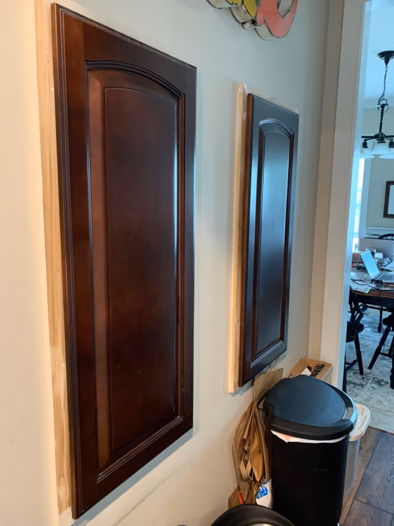 Dark wood kitchen cabinet doors with curved panel design, under renovation, visible trash can and unfinished wall