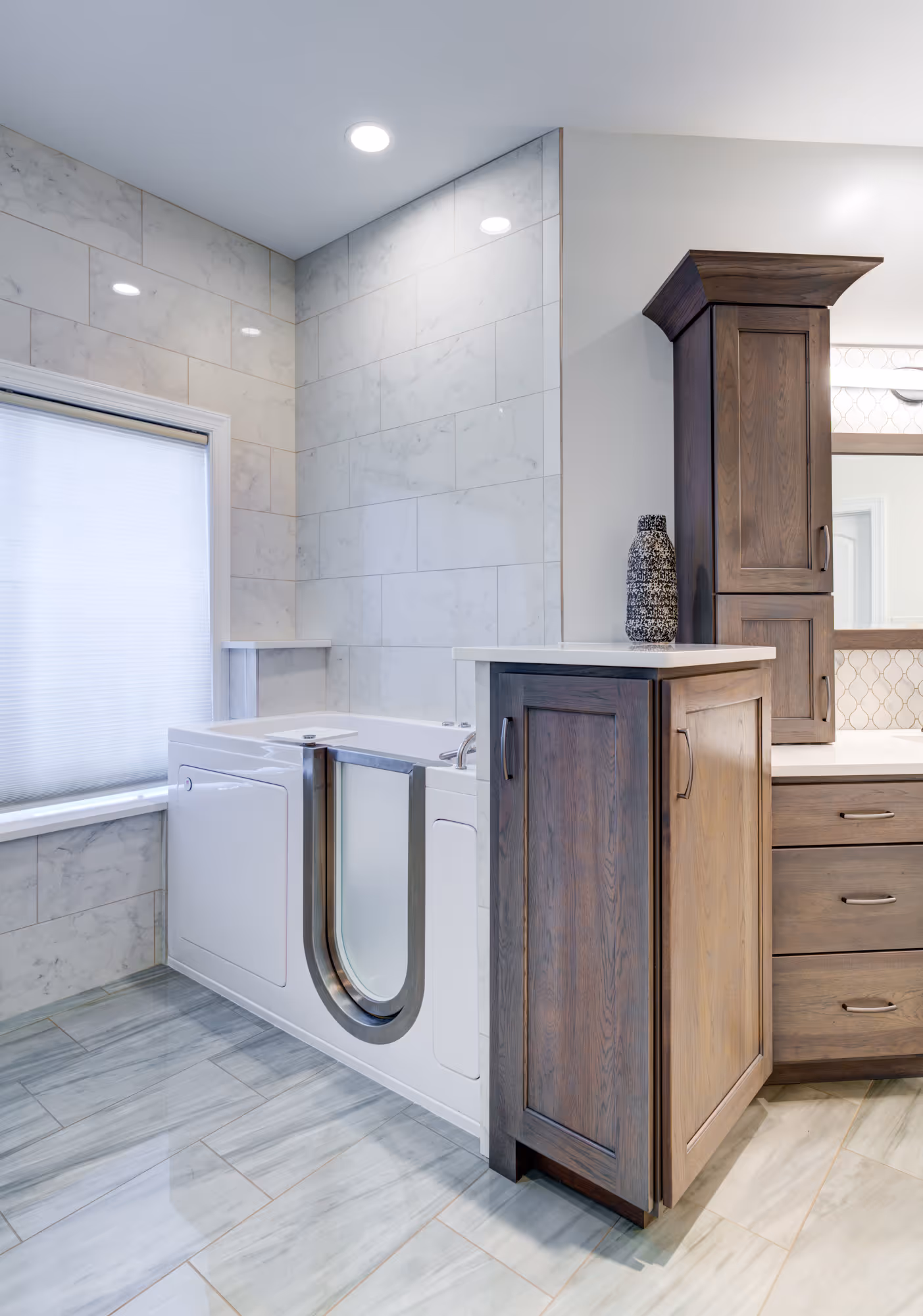 Modern bathroom in Mechanicsburg, PA featuring a walk-in tub, marble tiles, and dark wood cabinetry for accessible design.