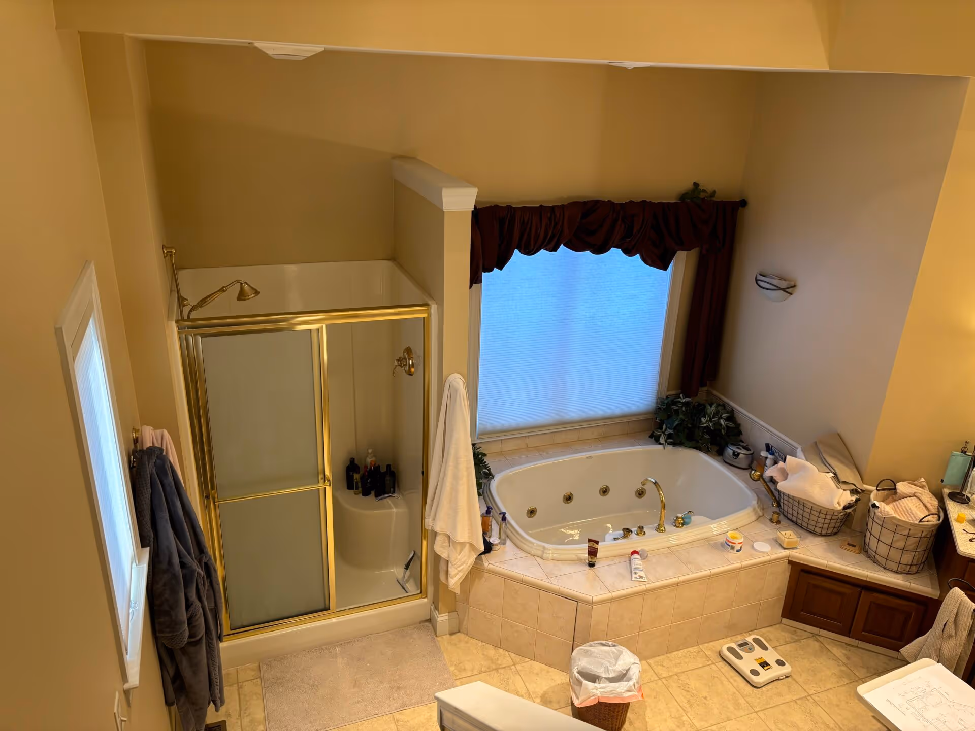 Before photo of a primary bathroom with a freestanding tub and shower in Mechanicsburg, PA, featuring beige walls and a gold-framed shower.