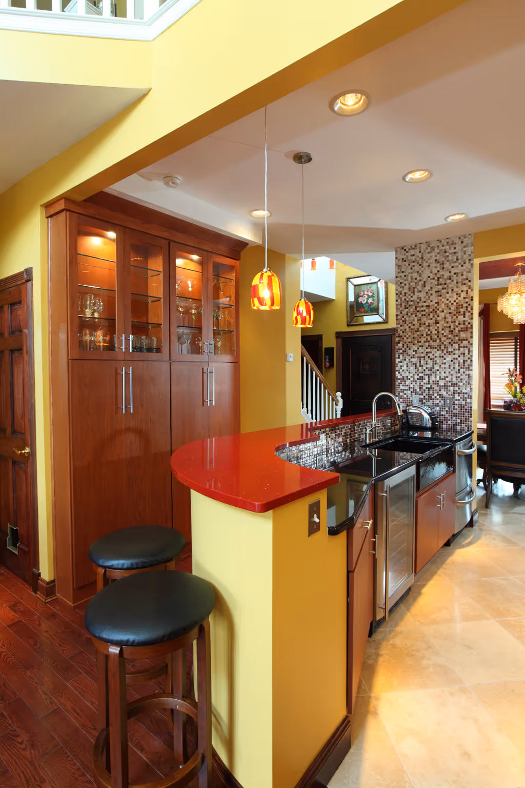 Modern kitchen in Harrisburg, PA featuring red quartz countertop, glass cabinetry, and vibrant yellow walls.
