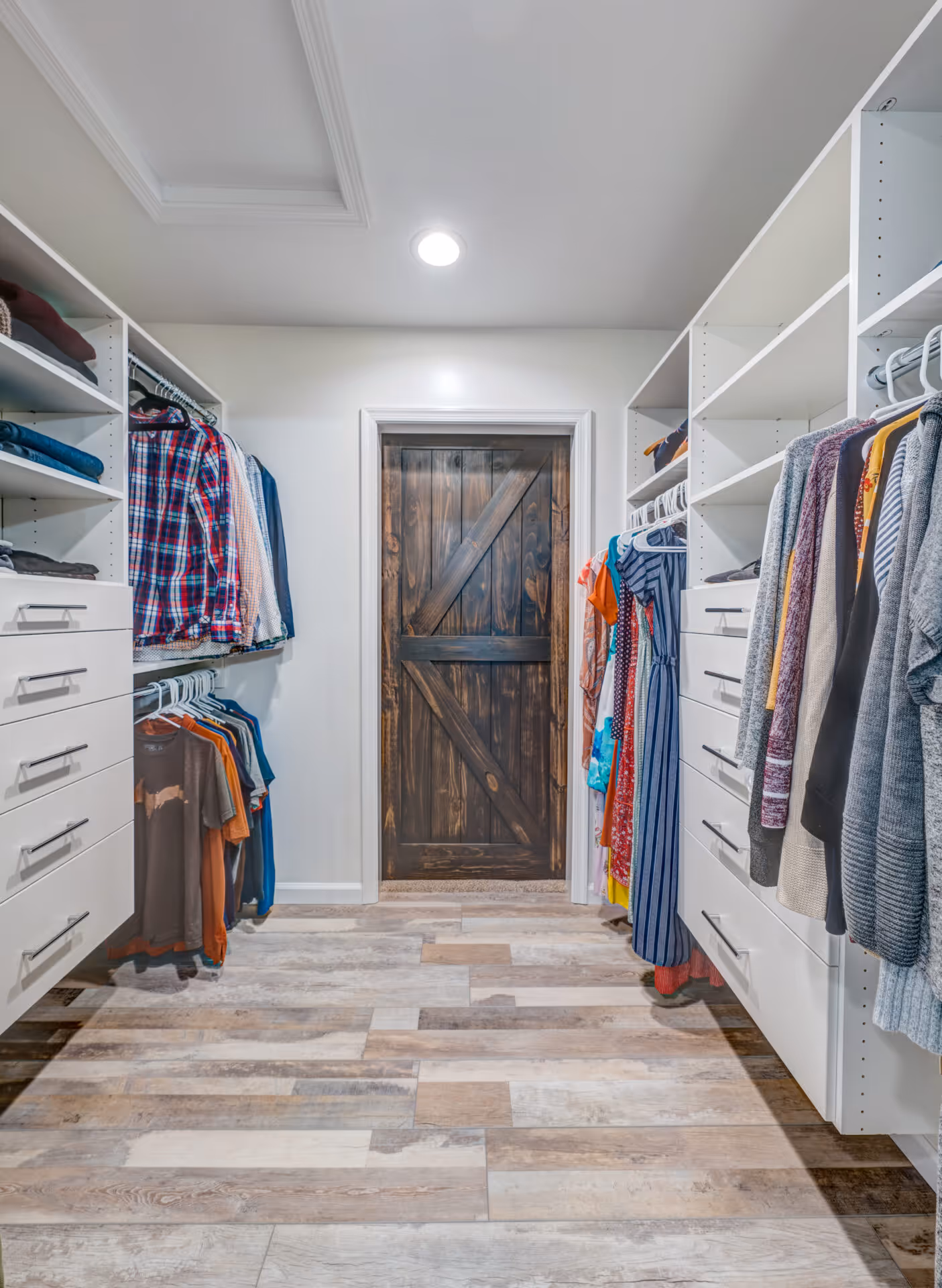 Spacious walk-in closet featuring white cabinetry, hanging clothes, wooden flooring, and a barn-style door in Elizabethtown, PA.