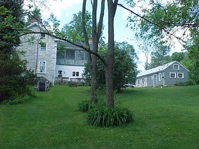 A charming exterior view of a two-story stone house and a gray shed surrounded by lush green grass in Boiling Springs, PA.