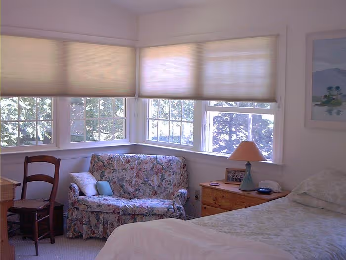 Cozy bedroom in Boiling Springs, PA featuring a floral loveseat, large windows, and a bedside lamp.