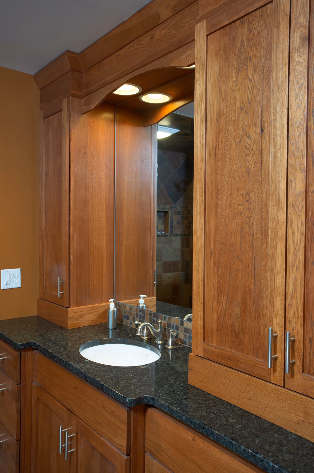 Transitional bathroom with wood cabinets, black granite countertop, and modern fixtures in Camp Hill, PA.