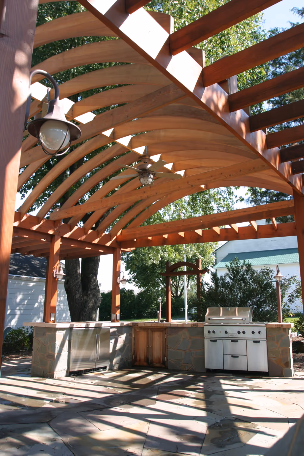 Stunning outdoor kitchen with stone countertop and wooden pergola in Harrisburg, PA, featuring built-in grill and stainless steel appliances.