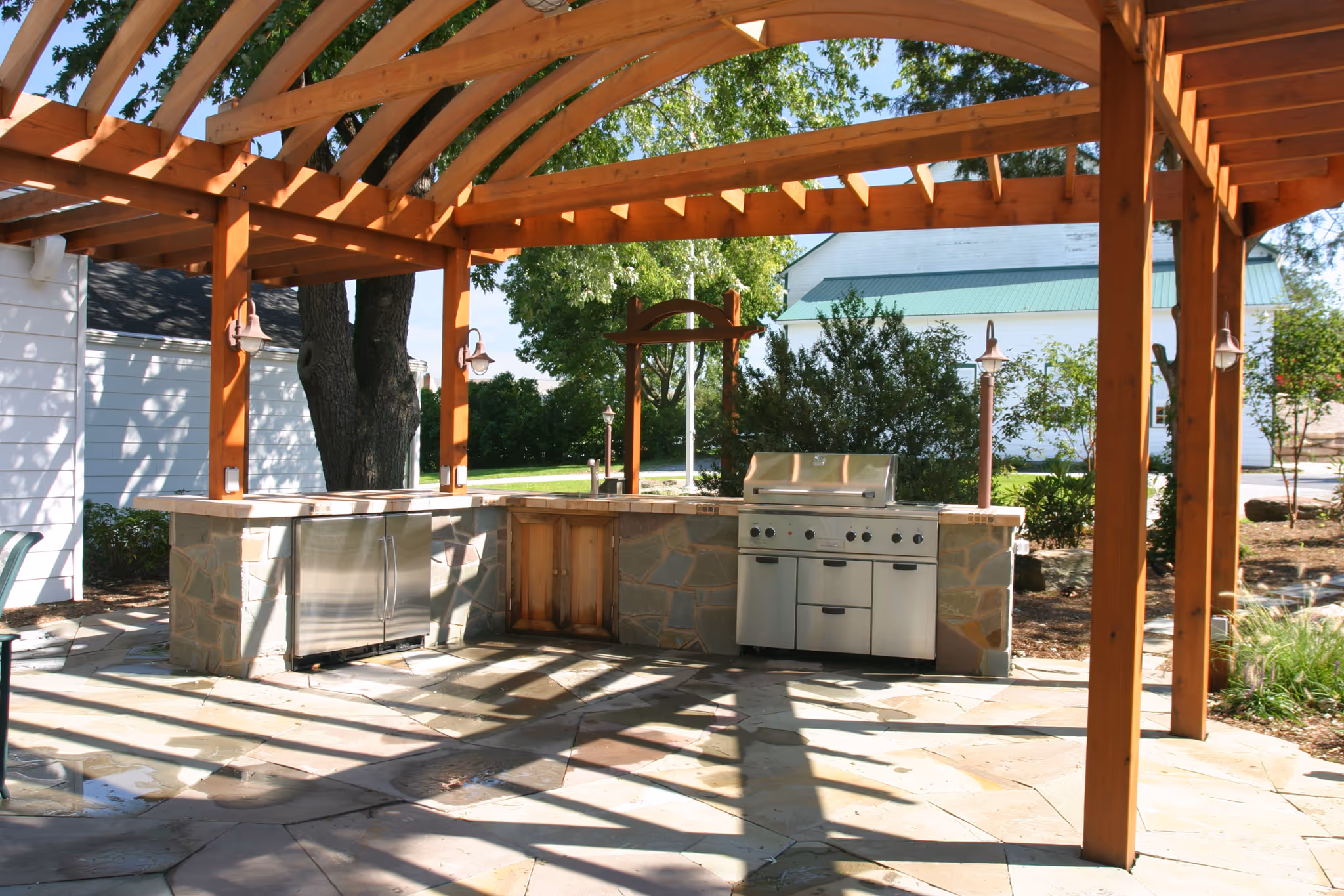 Outdoor kitchen with stainless steel grill and stone countertop under wooden pergola in harrisburg, pa
