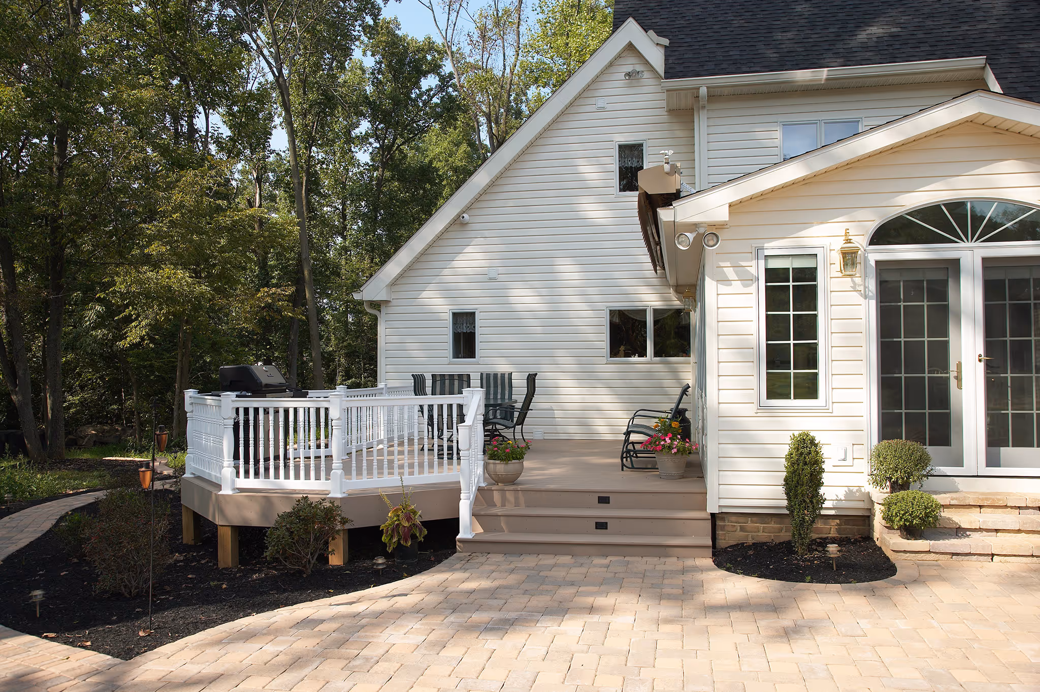 Contemporary outdoor deck with white railing, paver patio, and lush greenery in middletown, pa