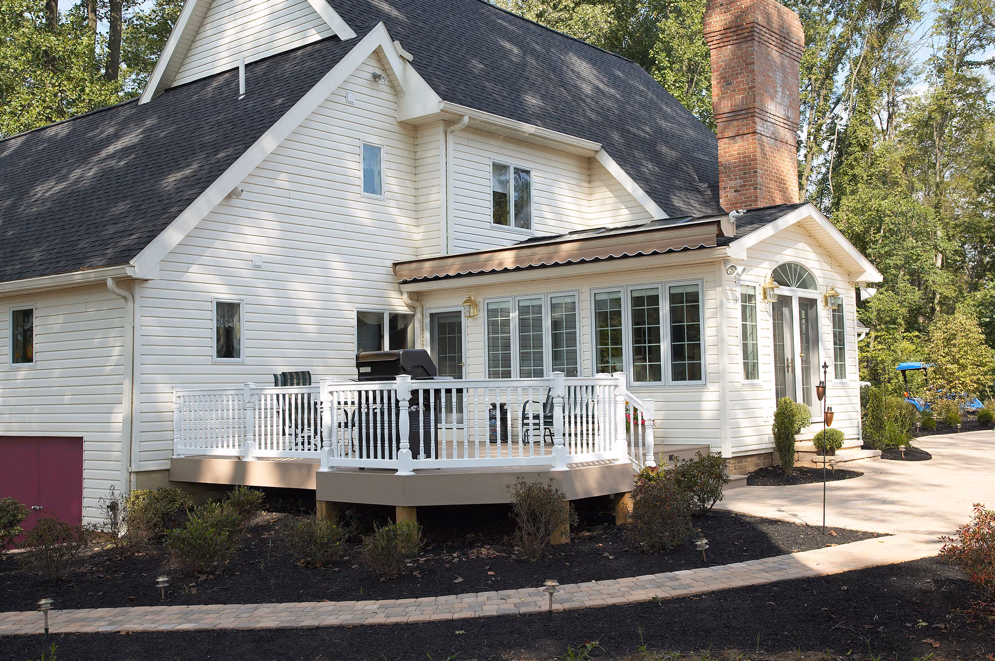 Modern exterior view of a house in Middletown, PA featuring a white deck, brick chimney, and lush landscaping