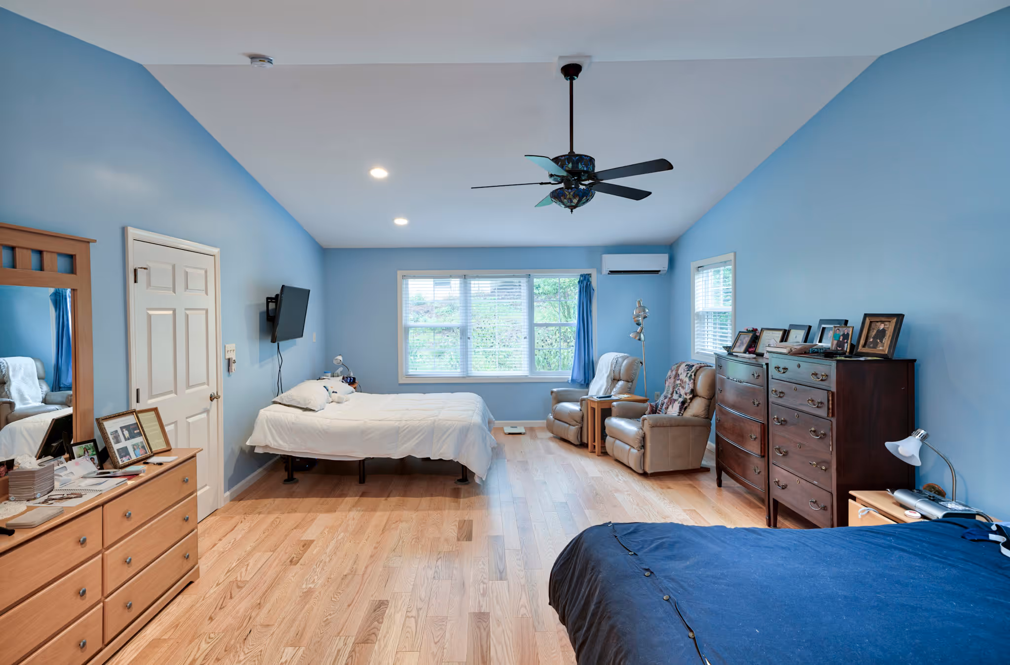 Spacious blue bedroom featuring wooden flooring, a ceiling fan, and two comfortable chairs. Located in Mechanicsburg, PA.