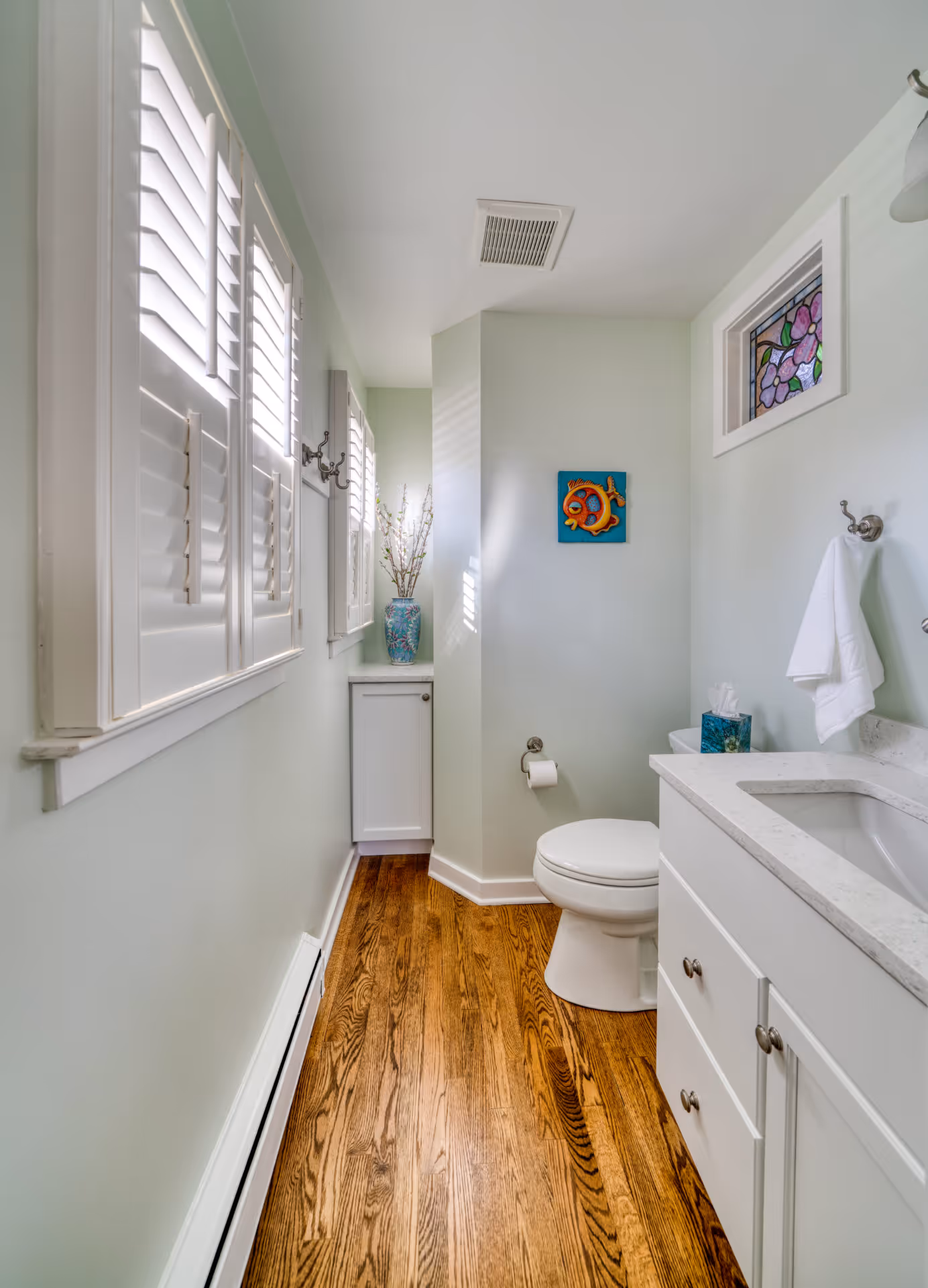 Charming transitional powder room with light green walls, white fixtures, and wooden flooring in Camp Hill, PA.