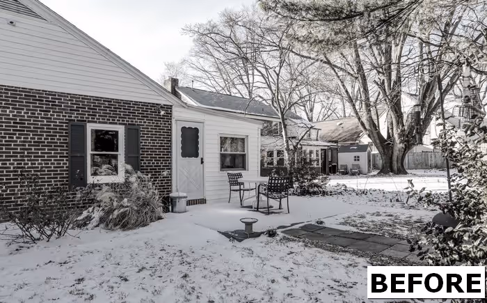 Before renovation view of a winter backyard in Camp Hill, PA featuring a brick house and chairs in the snow.