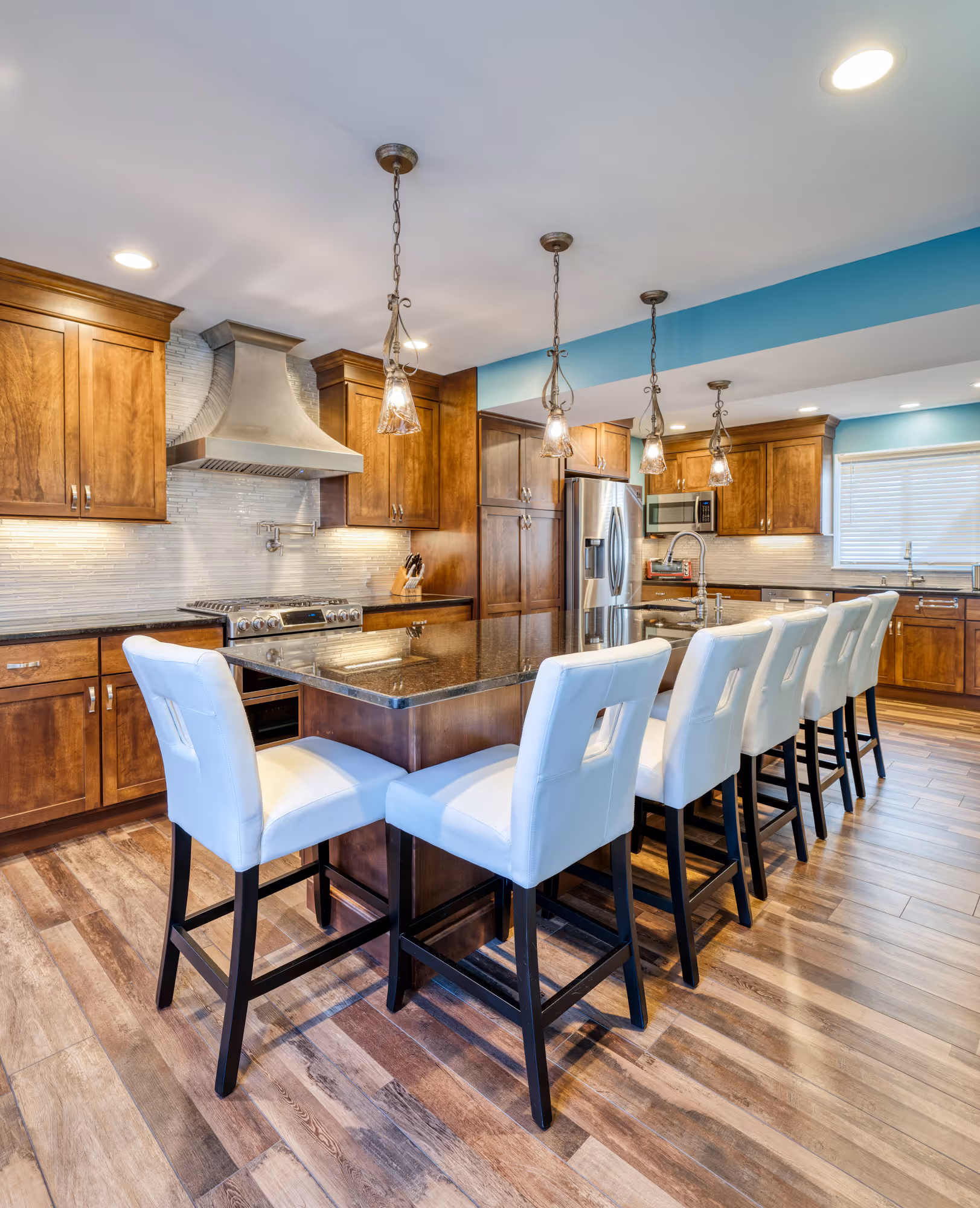Modern kitchen design in Hershey, PA featuring wood cabinets, granite island, and white bar stools.