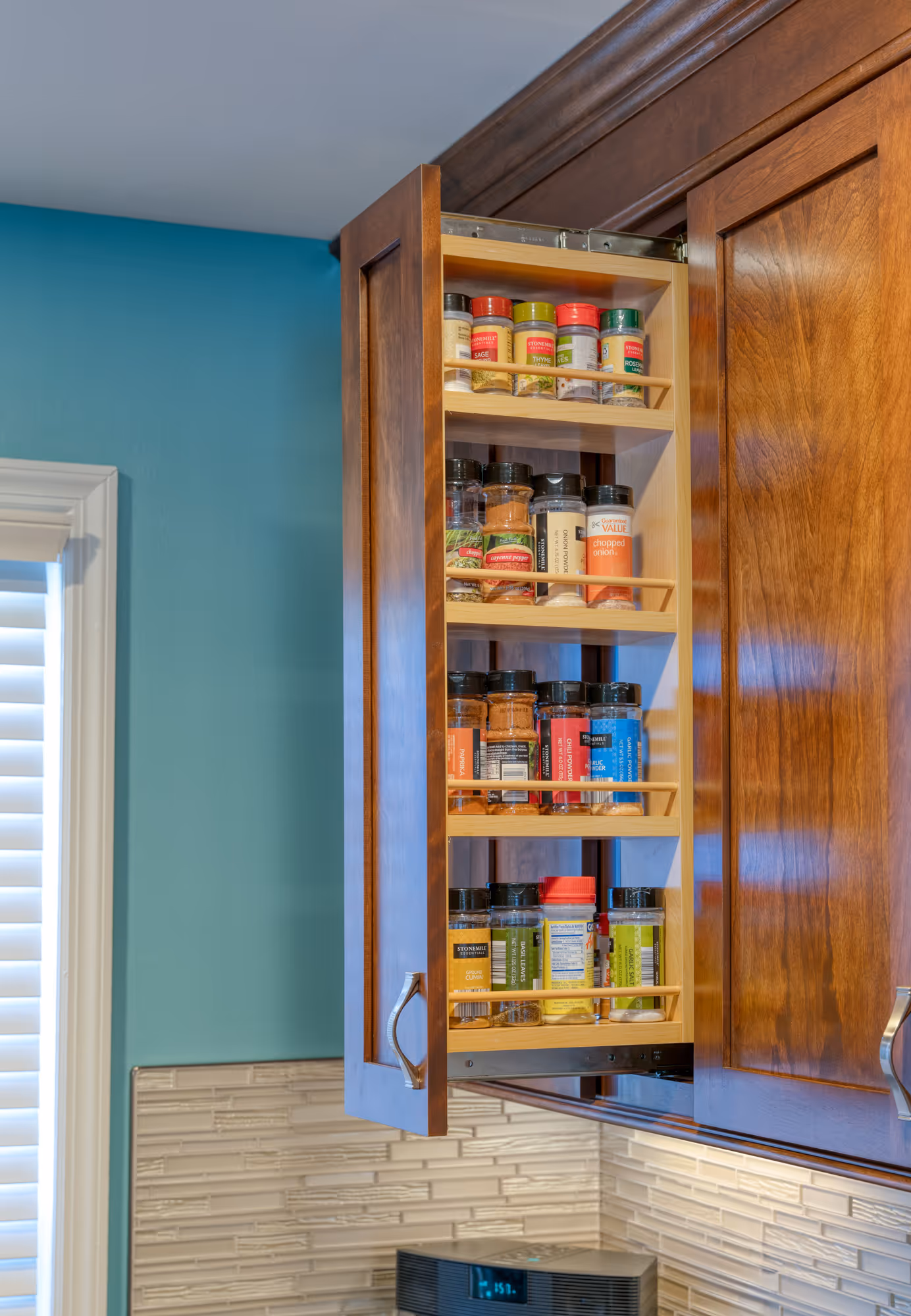 Kitchen in Hershey, PA featuring a hidden pull-out spice rack with organized spice jars and teal wall accents.