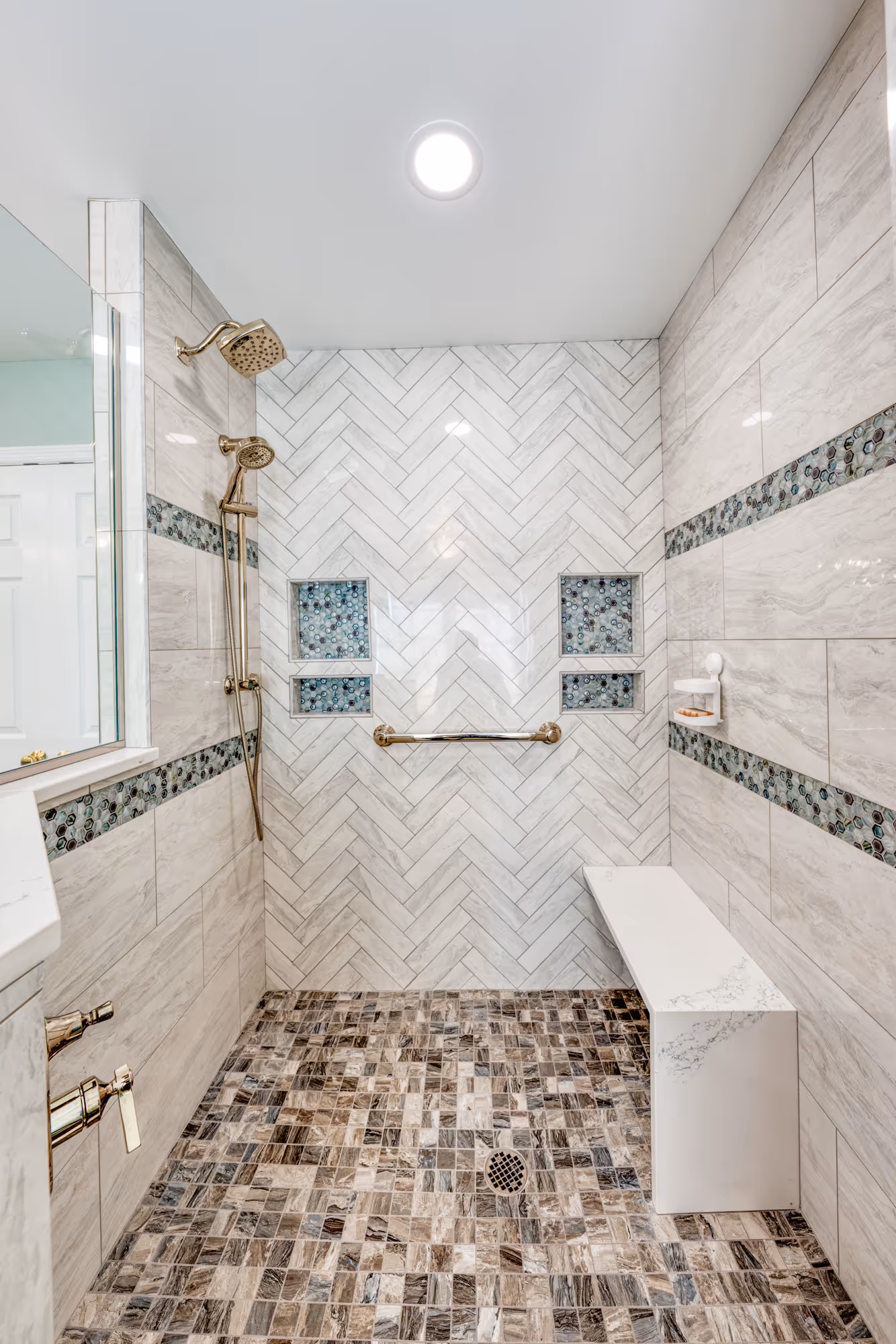 Luxurious modern bathroom shower with herringbone subway tile, mosaic accents, and marble bench in Enola, PA.
