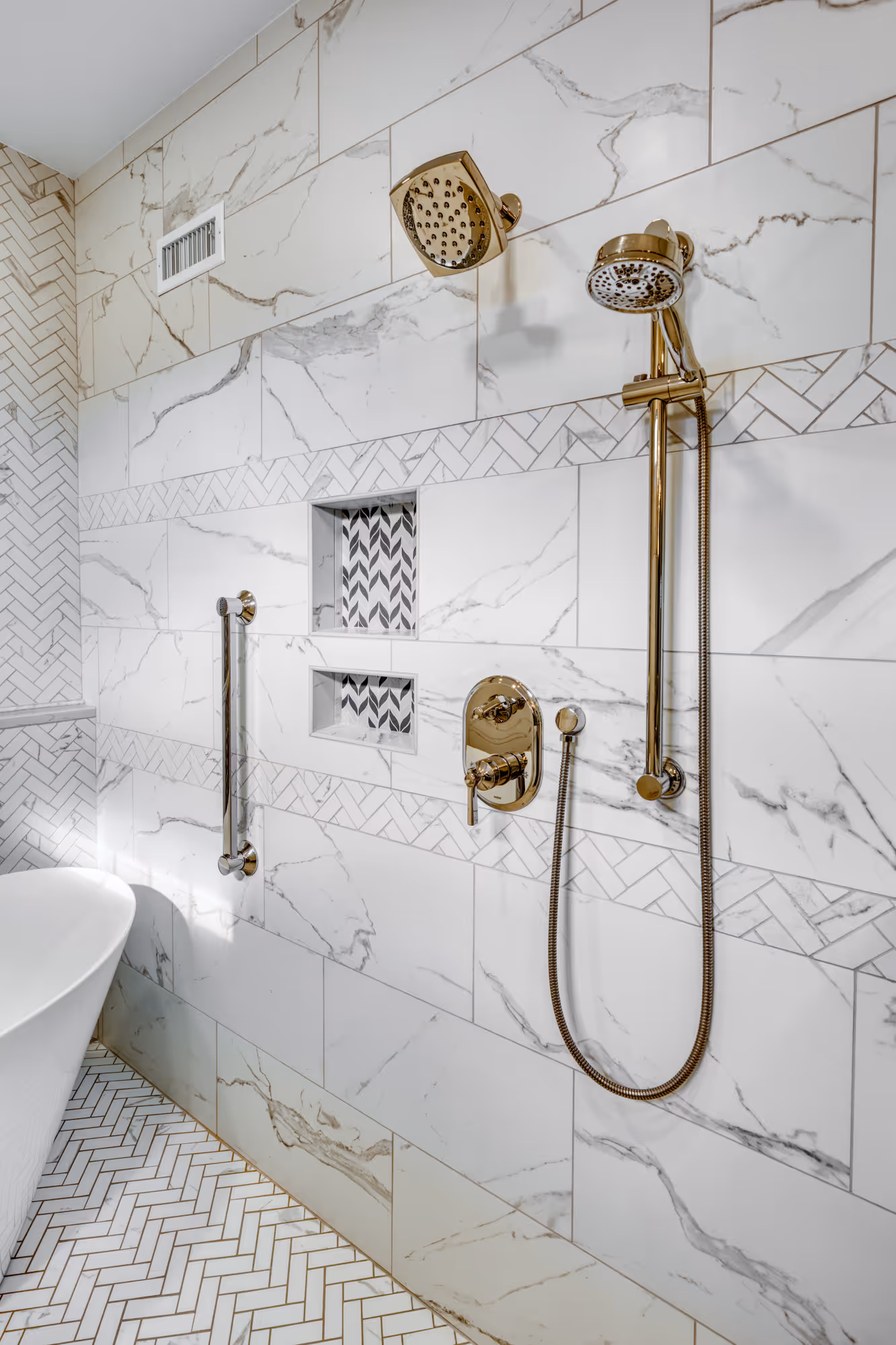 Luxury bathroom in Camp Hill, PA featuring gold shower hardware, marble tiles, and a freestanding bathtub.
