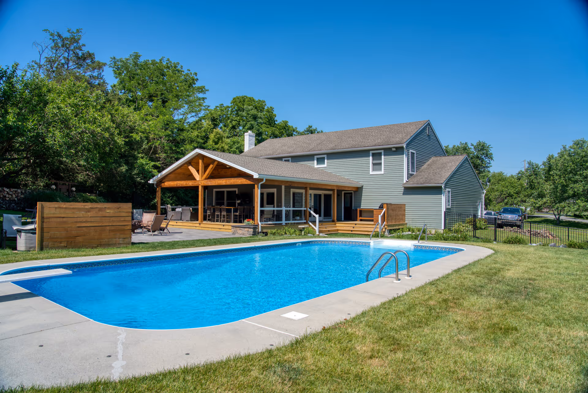 Modern backyard with a swimming pool and covered patio in Dillsburg, PA featuring wooden beams and outdoor seating.