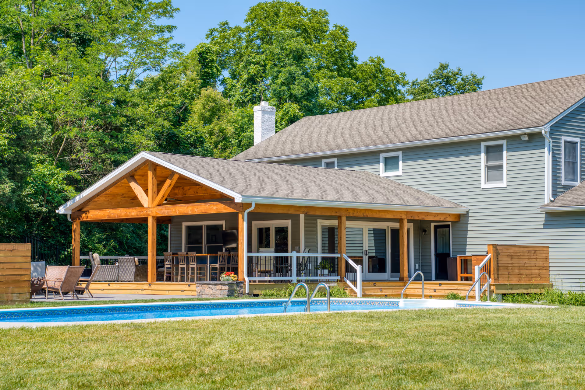 Transitional outdoor living area with wooden pergola and swimming pool in Dillsburg, PA, featuring modern furniture and green landscaping.