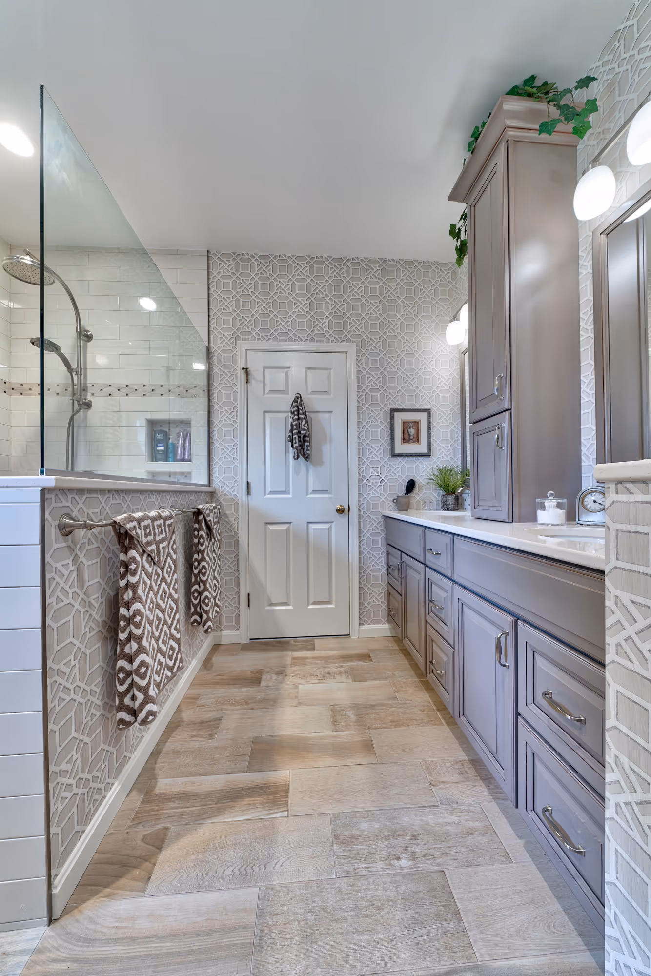Modern bathroom in Hershey, PA featuring wood tile floor, decorative wallpaper, and stylish cabinetry.