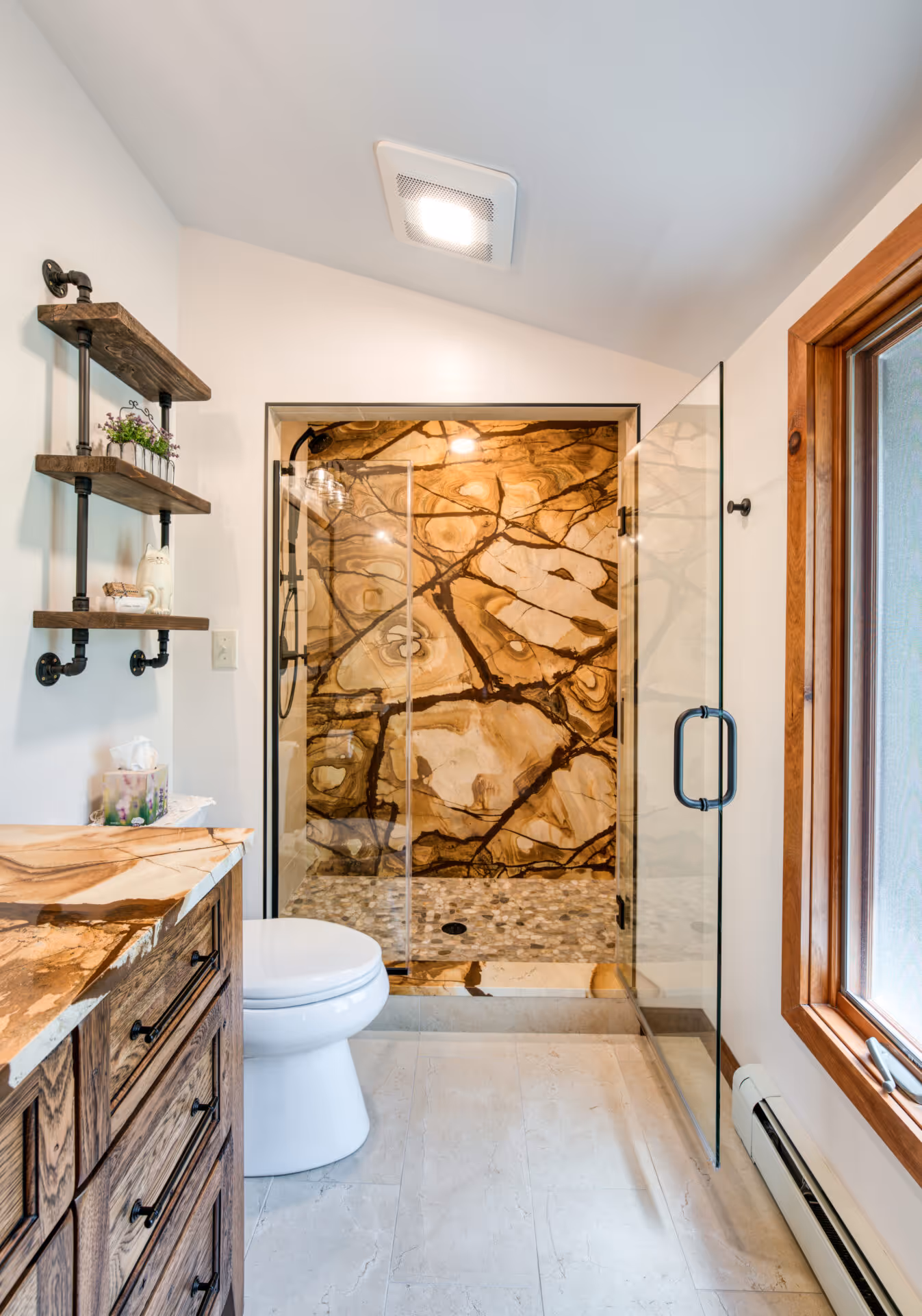 Modern bathroom in Dillsburg, PA featuring a glass shower, wooden vanity, and decorative shelves.