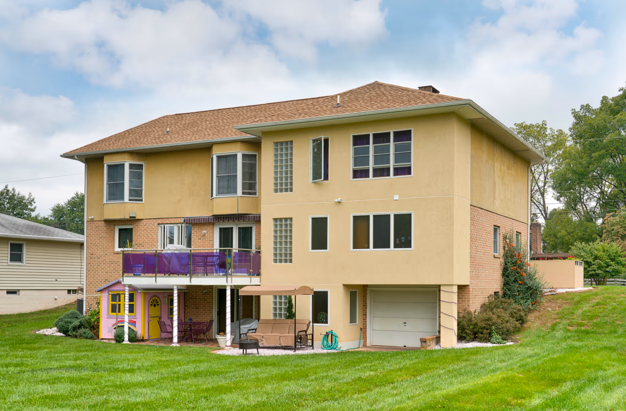 Contemporary exterior of a two-story house with a balcony, lush lawn, and vibrant children’s playhouse in Camp Hill, PA.