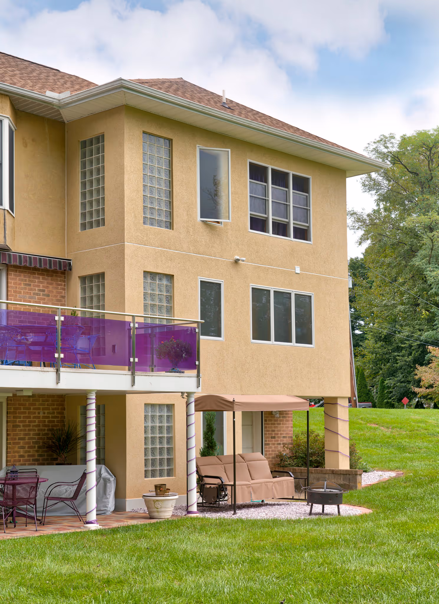Contemporary exterior of a home in Camp Hill, PA, featuring a purple balcony, outdoor seating, and lush green lawn.